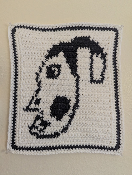 A black and cream crocheted tapestry showing an expressive face